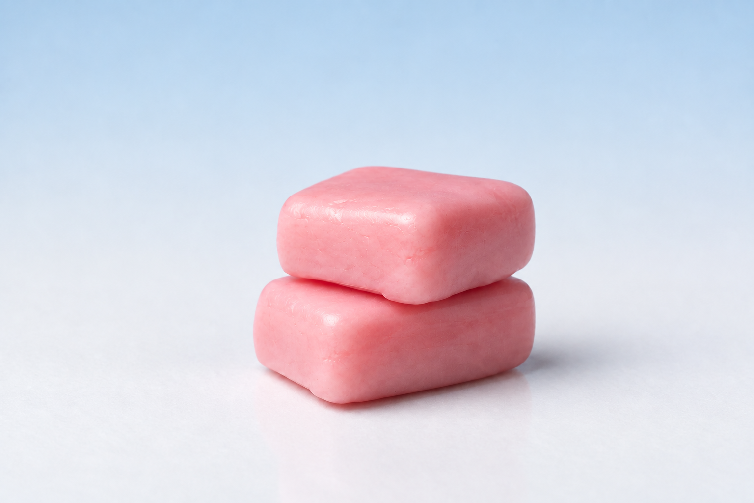 Two unwrapped strawberry-pink Stage 2 soft chews stacked on a white-to-pale-blue studio surface